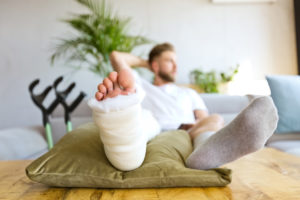 A man sitting down with his leg and foot elevated while it's in a cast since he's sustained an injury.